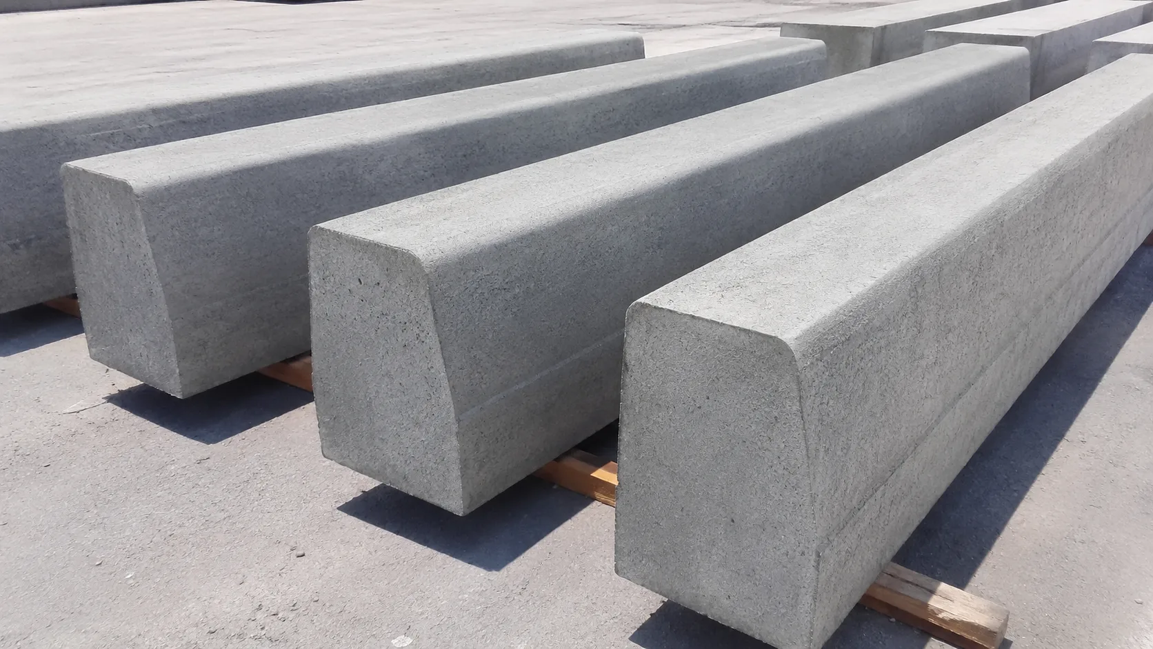 Temiz bir stok alanında düzenli şekilde sergilenen, büyük ve ağır tip gri beton karayolu bordür taşlarının fotogerçekçi ürün görseli.